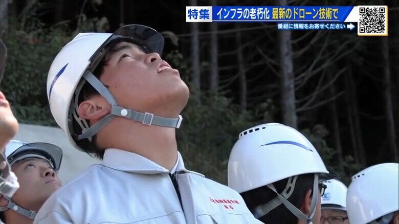 現場上空のドローンを見上げる高校生たち