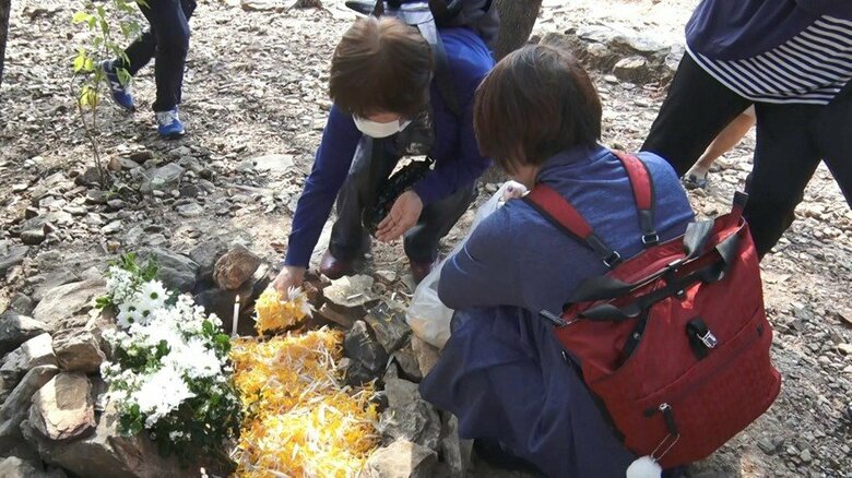 丘の中腹に設けられた智子さんのための石碑　線香を供え、囲いには丁寧に花が敷き詰められた