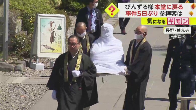 白い布で覆われた像が2人掛かりで運ばれている