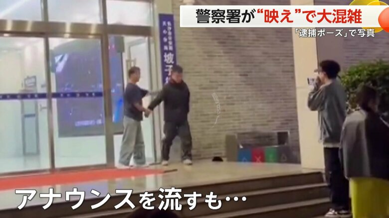 警察署の前での腕を拘束されたようなポーズでの記念撮影する人