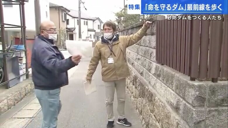 自宅の塀の高さまで土砂が来た写真を見せる河本さん（左）と矢野記者（右）