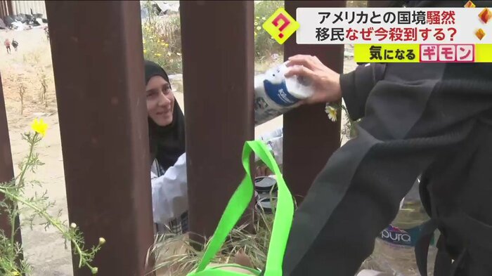 国境の壁の隙間から生活用品や食料を運び込む様子