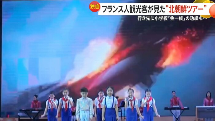 子どもたちの歌うステージのスクリーンには撃ち落とされる戦闘機などの映像が
