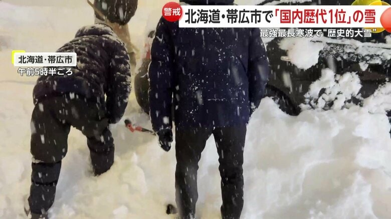 雪で動けなくなった車の周りの除雪作業が行われている様子