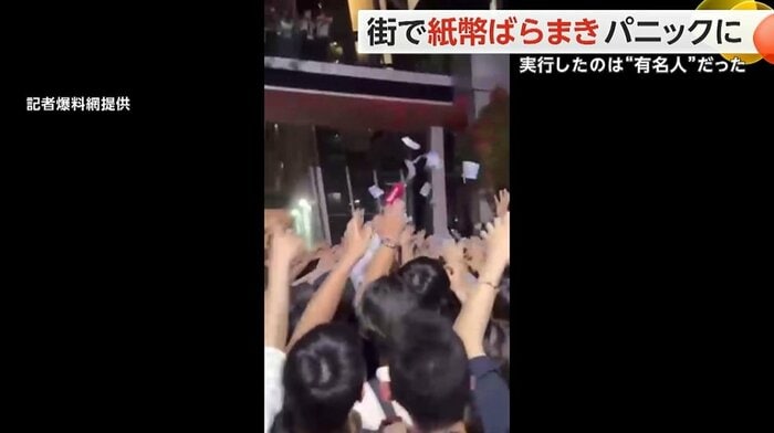 大勢の人が押し寄せる中、紙幣が舞っている