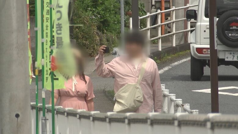 小学校のほうにスマートフォンを向けて写真撮影をする外国人観光客