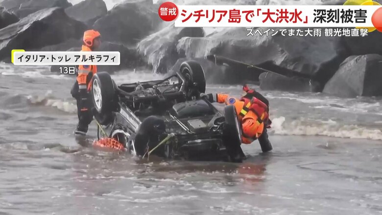海に漬かった状態で横転する車　その近くでは、救助隊員が中に人がいないかなどを確認している様子が